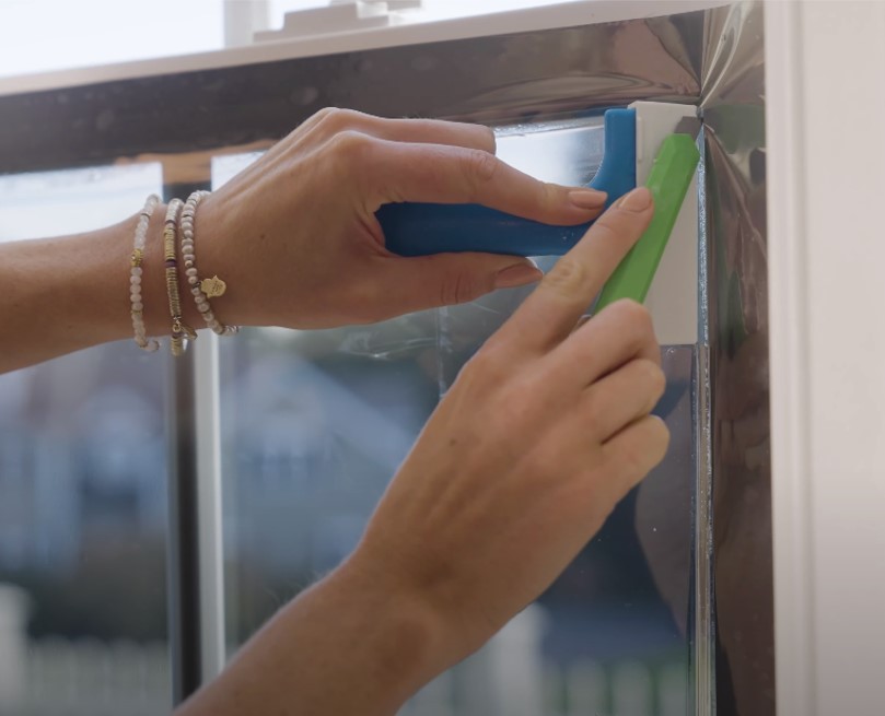 Photo of a woman trimming window film as part of a DIY installation in her home.