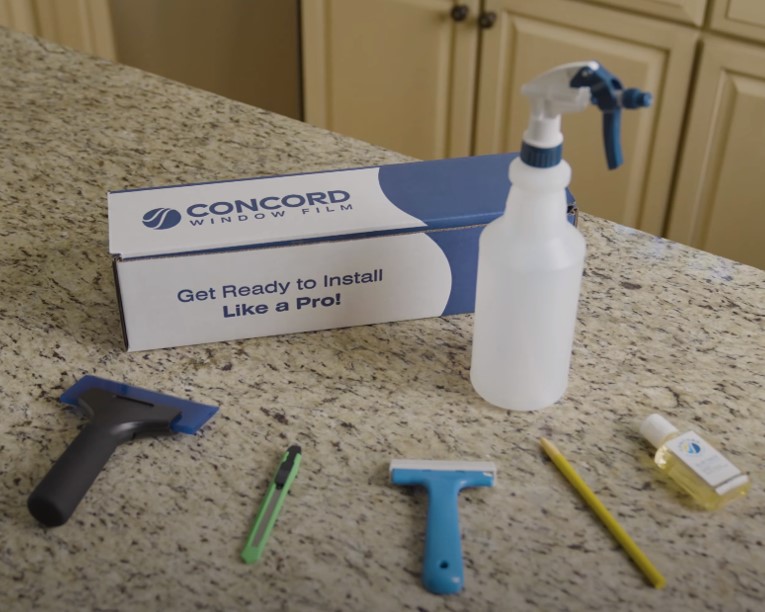Window tinting tools that come in Concord Window Film's Installation Tool Kit arranged on a counter with the box present.
