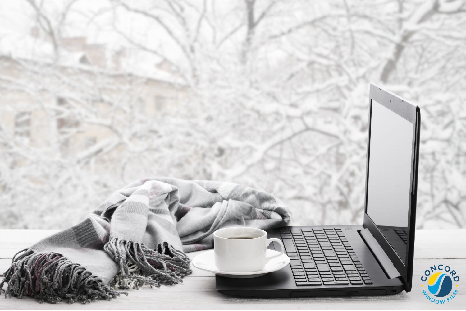 Photo of a desk with a laptop on it in front of a window with snow falling outside for a post on low-E windows
